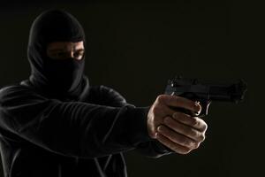 The robber in a mask with a gun pointed to the side on a black background photo