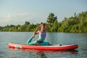 Young woman doing yoga on sup board with paddle. Meditative pose, side view - concept of harmony with the nature photo