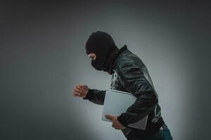 Thief stealing a laptop computer. Isolated on gray background photo