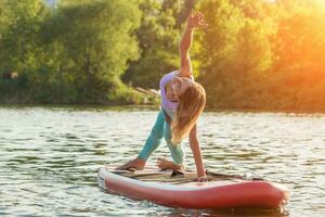 Young woman doing yoga on sup board with paddle. Yoga pose, side view - concept of harmony with the nature. photo