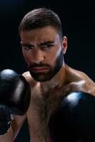 Portrait of tough male boxer posing in boxing stance against black background. photo
