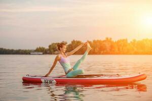 Young woman sitting on paddle board, practicing yoga pose. Doing yoga exercise on sup board, active summer rest photo