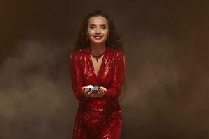 joven bonito suerte morena mujer en un rojo noche vestir sostiene póker papas fritas en su manos, demostración su ganancias. foto