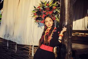 Brunette girl in a white ukrainian authentic national costume and a wreath of flowers is posing against a terrace. photo