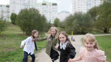 en grupp av liten Lycklig flickor spelar i en stad parkera löpning och skrattande längs de väg långsam rörelse video