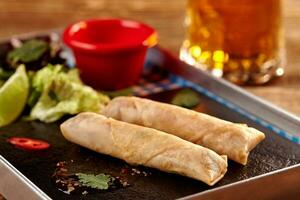 Spring rolls with sweet chili sauce, salad and beer on wooden table. photo