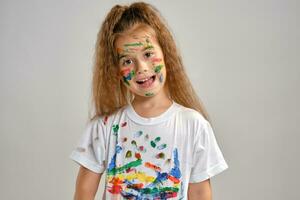 pequeño niña en blanco camiseta, con pintado cara es haciendo muecas mientras posando aislado en blanco. Arte estudio. de cerca. foto