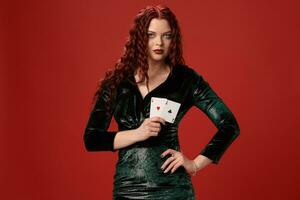 joven sexy mujer con un rojo Rizado pelo participación ases, en un rojo antecedentes. póker foto