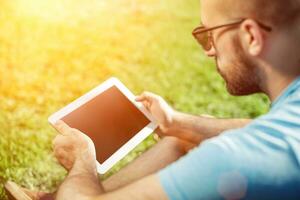 Young man using and typing tablet computer in summer grass. photo