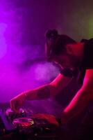 Attractive young DJ playing on turntables with color light effects photo