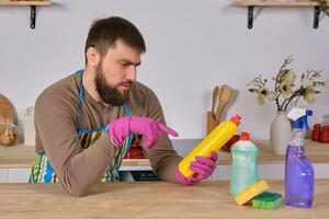 Young man wanted to help his wife in housecleaning, but he doesn't know what to do with all of detergents photo