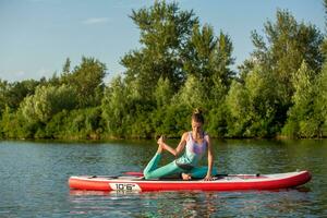 Young woman doing yoga on sup board with paddle. Meditative pose, side view - concept of harmony with the nature photo