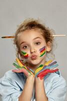 hermosa pequeño niña con un pintado manos y las mejillas es posando en un gris antecedentes. foto