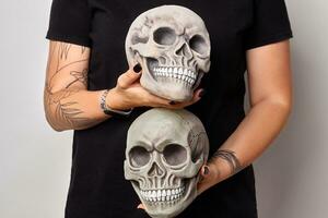 Tattooed hands of a woman in a black watch and clothes are holding a realistic model of a human skulls with teeth isolated on white. Close-up shot. photo