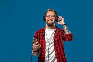 contento joven hombre escuchando a música con auriculares. hermoso sonriente chico en a cuadros camisa con cerrado ojos bailando con auriculares. foto