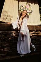 Brunette girl in a white ukrainian authentic national costume and a wreath of flowers is posing against a terrace. photo