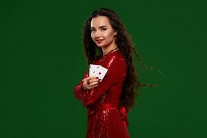 Young beautiful lucky brunette in a red evening dress shows her cards, a pair of aces on green background photo