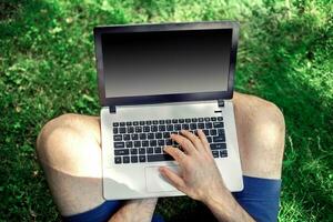 Young blogger sitting on grass and working with laptop photo