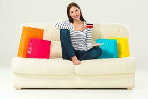 Young woman with credit card buying sitting on sofa with paper bags and new clothes photo