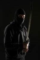 Man with balaclava and katana sword on black background photo