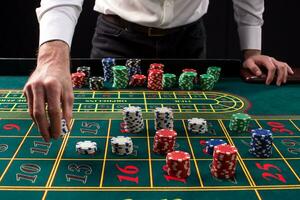 A close-up vibrant image of green casino table with roulette, with the hands of croupier and multicolored chips. photo