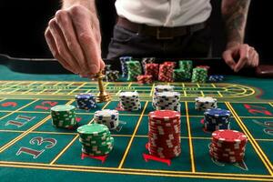 A close-up vibrant image of green casino table with roulette, with the hands of croupier and multicolored chips. photo