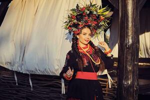 Brunette girl in a white ukrainian authentic national costume and a wreath of flowers is posing against a terrace. photo