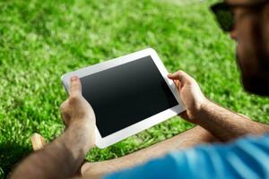 Young man using and typing tablet computer in summer grass. photo