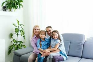 alegre joven familia con niños riendo sentado en sofá juntos, padres con niños disfrutando entretenido a hogar foto