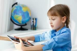 inteligente pequeño Chica de escuela con digital tableta en un aula. niño en un elemental escuela. educación y aprendizaje para niños. foto