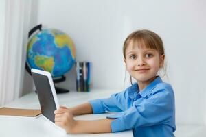 Cute little girl is sitting at table with her laptop and studying online photo