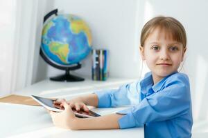 inteligente pequeño Chica de escuela con digital tableta en un aula. niño en un elemental escuela. educación y aprendizaje para niños. foto