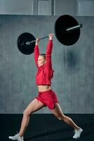 Strained young sportswoman ready to perform shoulder press exercise with heavy barbell photo