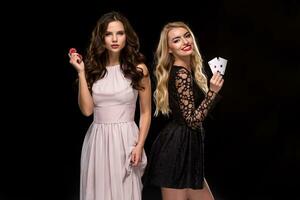 Two Sexy girls brunette and blonde, posing with chips and cards in their hands, poker concept black background photo