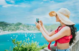 viajero niña fotografiando un bahía desde un punto de vista. contento turista mujer en un sombrero fotografiando un punto de vista, viaje y turismo promoción concepto foto