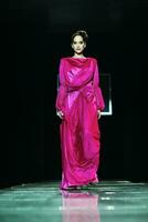 a woman in a pink gown walks down a runway photo