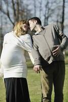 a pregnant woman and man kissing in a park photo