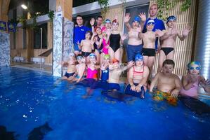 a group of children and adults posing for a photo in a swimming pool