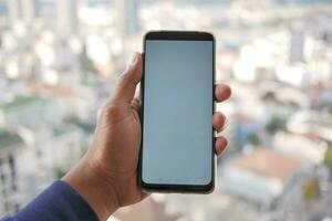 young man using smart phone with empty screen against city background photo