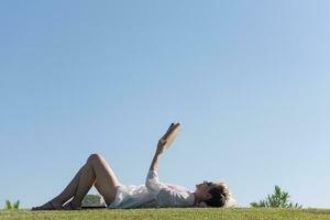 a woman laying on the grass reading a book photo