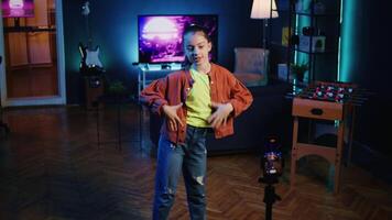 Panning shot of smiling kid taking part in viral dance trend after seeing favorite celebrities doing it, filming video with phone on tripod stabilizer, doing trendy challenge for online followers