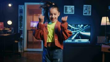 zoom in schot Aan vreugdevol dochter betoverend haar volgers met ongelooflijk dans beweegt in neon lit huis studio. klein media ster presentatie van koel dansen vaardigheden, filmen familie vriendelijk inhoud video