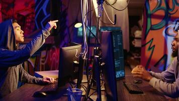 Zoom out shot of malicious men hacking, stealing credit card numbers and manipulating banking systems for their own personal gain. Evil hackers running code in graffiti painted basement video