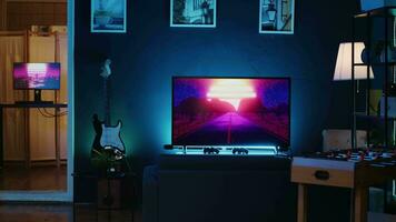 Panning shot of empty home studio illuminated with neon lights used for internet video production. Living room filled with content creation equipment, TV animations running in background