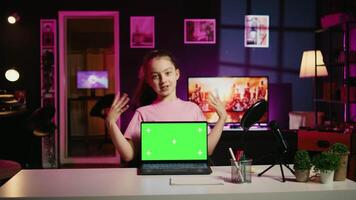 Young girl tech content creator filming technology review of green screen laptop, unboxing it and presenting specifications to audience. Cute gen Z influencer showing mockup notebook device to viewers video