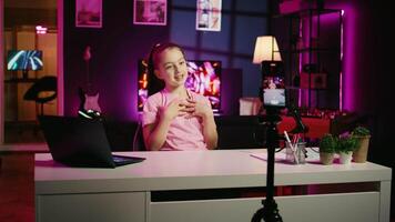 Zoom in shot of kid talking about school with children audience, filming content for social media with cellphone attached to tripod. Young girl recording video for internet channel with mobile phone