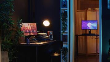 Work desk with computer and house plants in empty house interior with warm lighting. Living room illuminated by neon lights with 3D rendered animations running on powerful PC monitors video