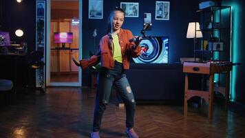 Panning shot of young media star dancing in apartment, recording video with phone on selfie stick for gen z internet fans. Excited kid filming herself with cellphone doing dance moves