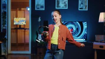 Child dancing and singing, using phone attached to selfie stick to shoot video for social media platforms in living room, doing professional filming techniques to entertain followers