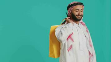 Happy arab holding shopping bags in studio, feeling cheerful after buying products on discount. Middle eastern person purchasing merchandise on sale at retail store, colorful paper bags. video